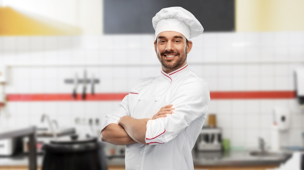 cooking, culinary and people concept - happy smiling male chef in toque and jacket over restaurant kitchen background. happy smiling male chef at restaurant kitchen