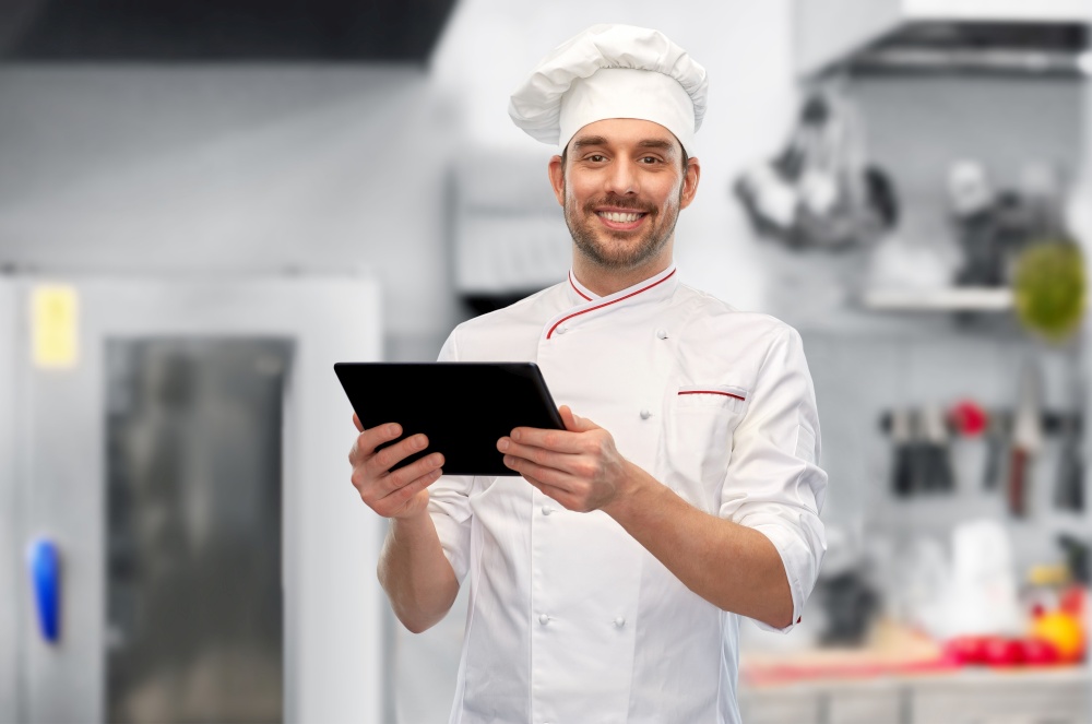 cooking, culinary and people concept - happy smiling male chef in toque with tablet pc computer over restaurant kitchen background. male chef with tablet pc at restaurant kitchen
