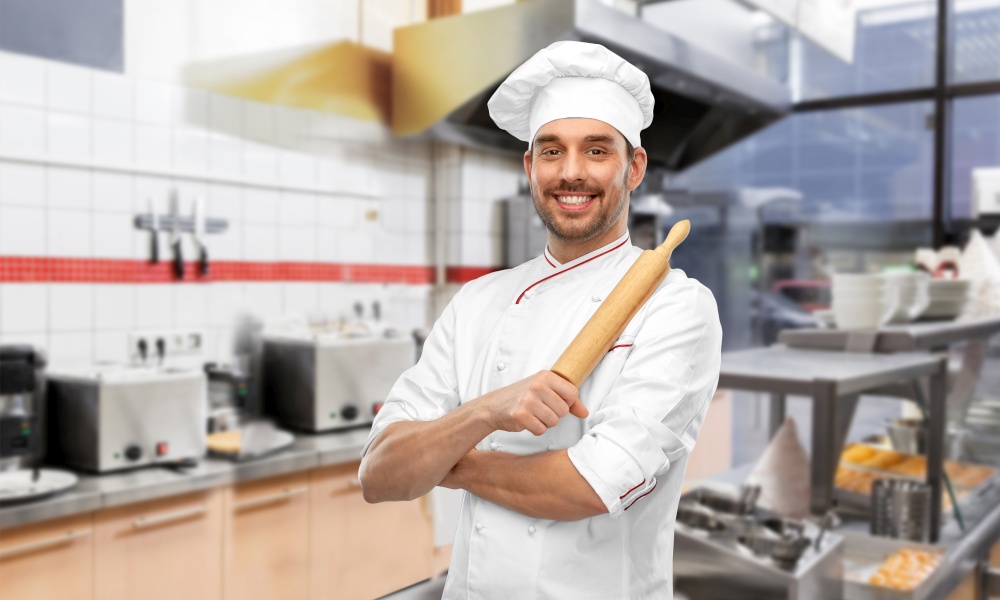 cooking, culinary and people concept - happy smiling male chef or baker in toque with rolling pin over restaurant kitchen background. happy male chef with rolling pin at kitchen