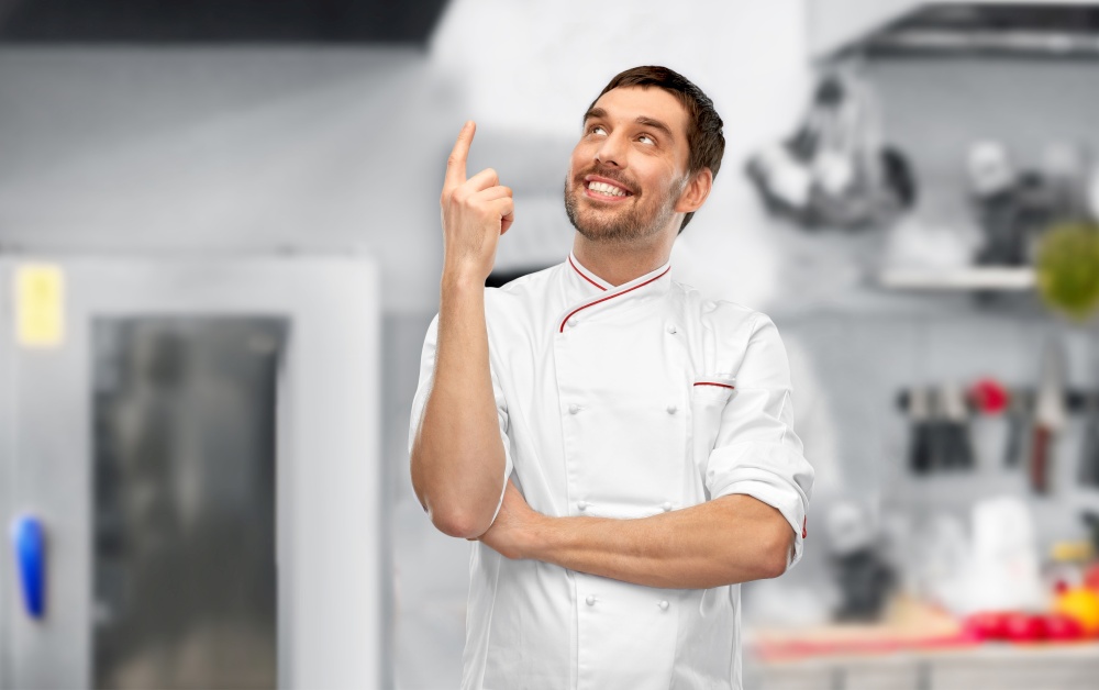 cooking, culinary and people concept - happy smiling male chef in jacket pointing finger up to something over grey background. happy smiling male chef pointing finger up