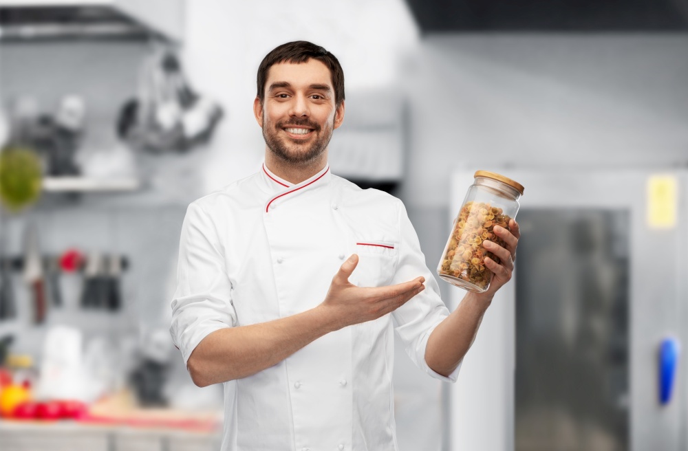 food cooking, culinary and people concept - happy smiling male chef in jacket with pasta in glass jar over grey background. happy smiling male chef with pasta in glass jar