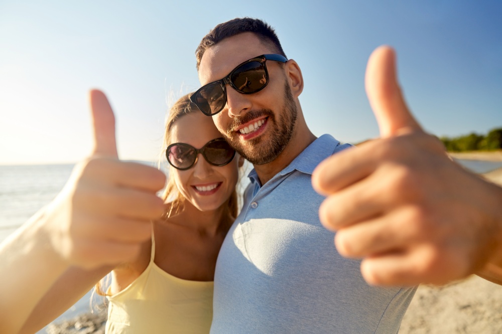 leisure, relationships and people concept - happy couple in sunglasses hugging and showing thumbs up on summer beach. happy couple showing thumbs up on summer beach