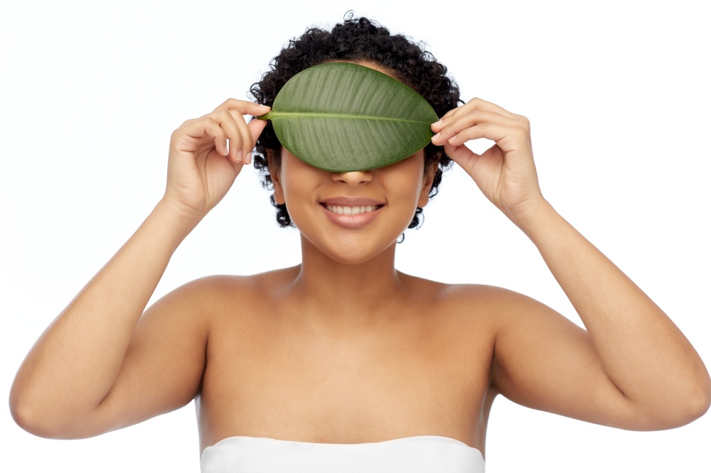 beauty, nature and people concept - portrait of happy smiling young african american woman with green leaf on her face over white background. portrait of african american woman with green leaf