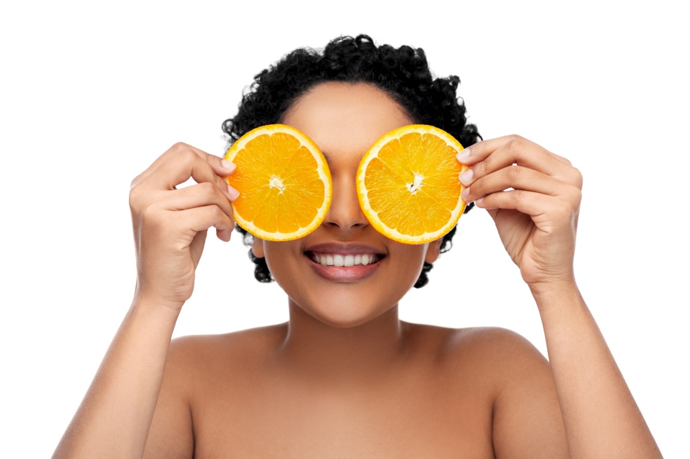 beauty, skin care and detox concept - smiling beautiful african american woman making eye mask of oranges over white background. smiling african woman making eye mask of oranges