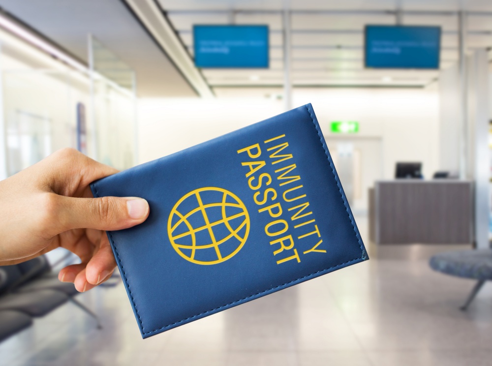 tourism, safe travel and health care concept - close up of hand holding immunity passport over airport background. close up of hand holding immunity passport