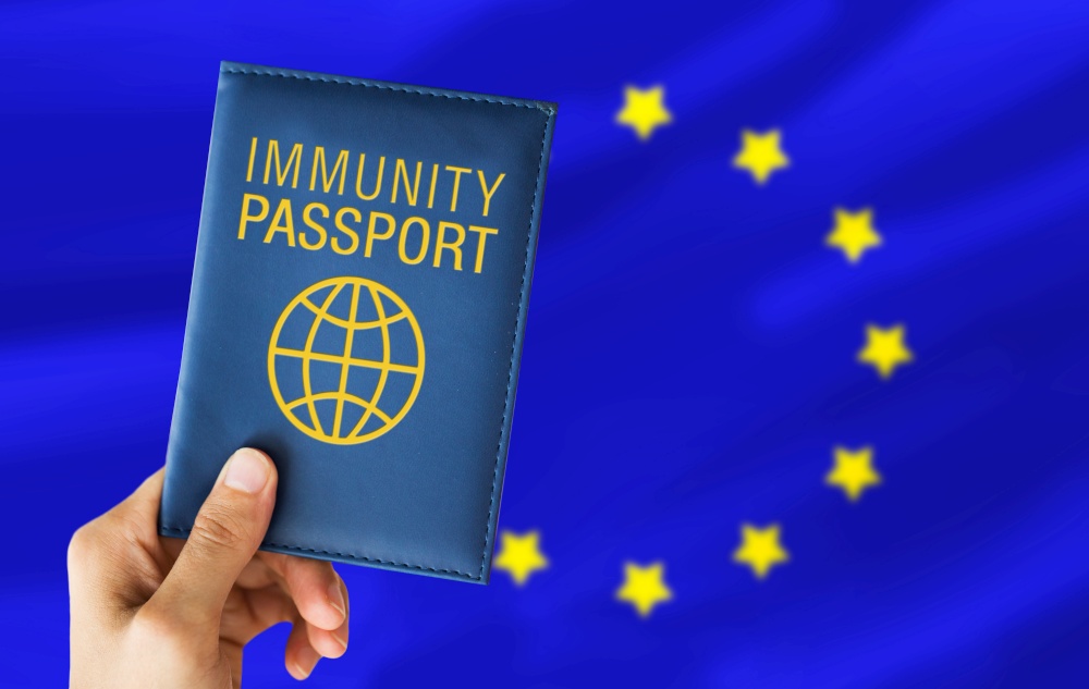 tourism, travel and health care concept - hand holding immunity passport over flag of european union on background. hand holding immunity passport over european union