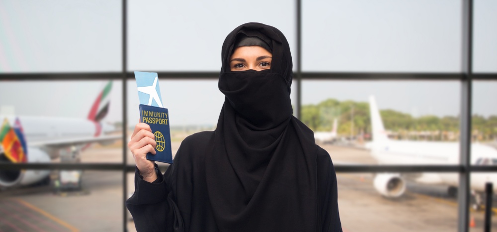 safe travel, tourism and people concept - muslim woman in hijab with air ticket and immunity passport over airport background. muslim woman with air ticket and immunity passport
