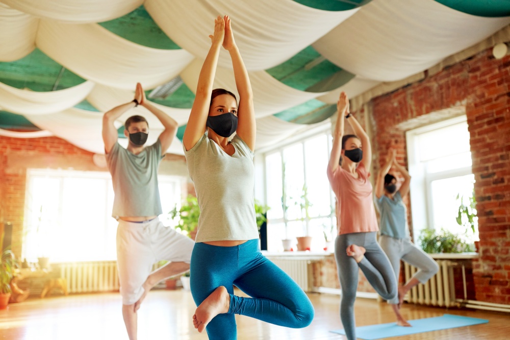 fitness, meditation and health care concept - group of people wearing black face protective masks for protection from virus disease doing yoga in tree pose at studio. group of people in masks doing yoga at studio