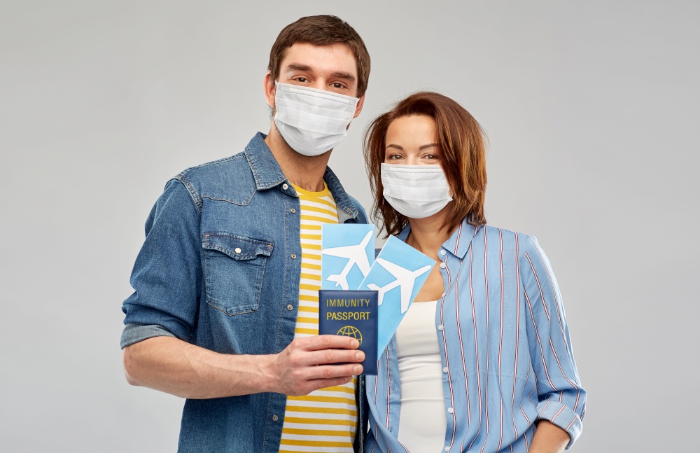 safe travel, tourism and vacation concept - couple in masks with air tickets, passport and camera over grey background. couple in masks with tickets and immunity passport