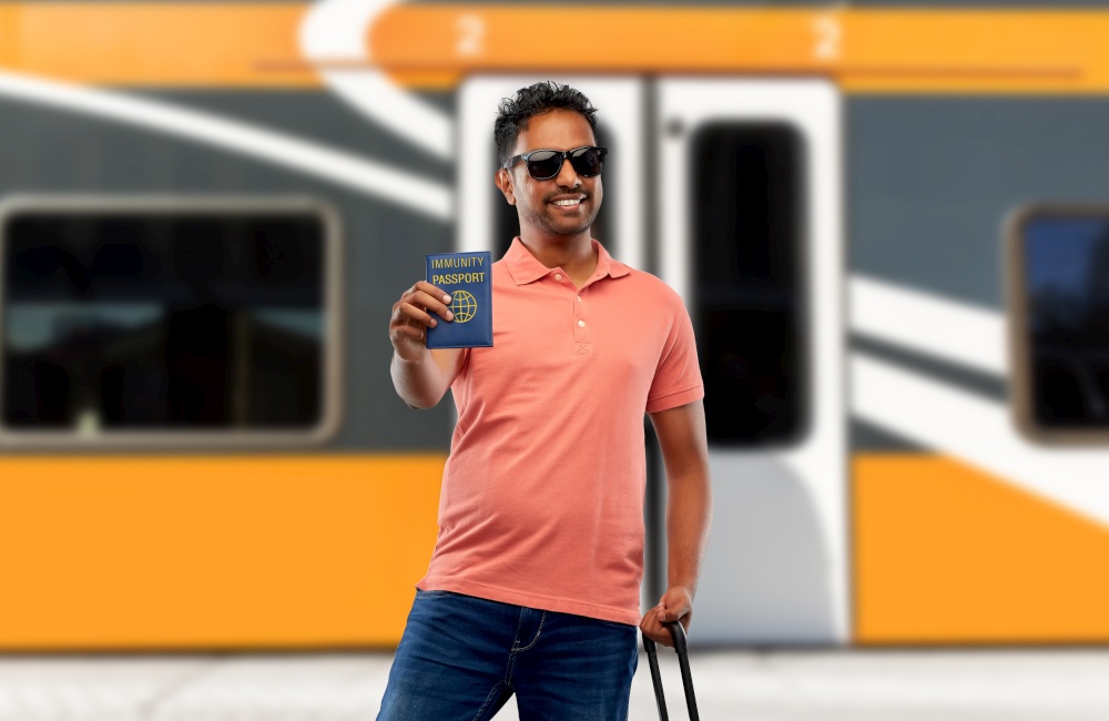safe travel, tourism and health care concept - happy smiling young indian man with air ticket, immunity passport and bag walking over train background. happy man with air ticket and immunity passport