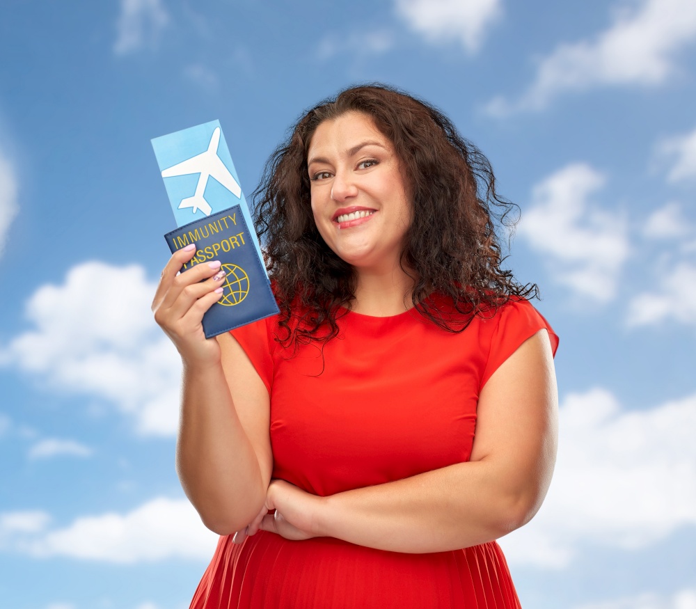 safe travel, tourism and vacation concept - happy woman in red dress with immunity passport and air ticket over blue sky and clouds background. happy woman with immunity passport and air ticket