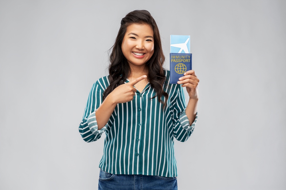 safe travel, tourism and health care concept - happy smiling young asian woman with air ticket and immunity passport over grey background. asian woman with air ticket and immunity passport