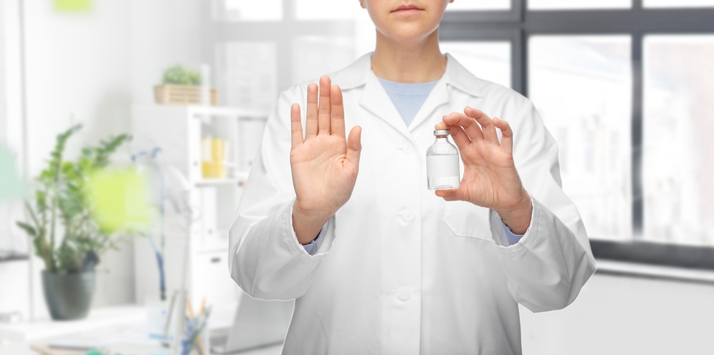 medicine, vaccination and healthcare concept - close up of female doctor or nurse with drug in bottle showing stop gesture over medical office at hospital background. doctor with syringe shows stop gesture at hospital