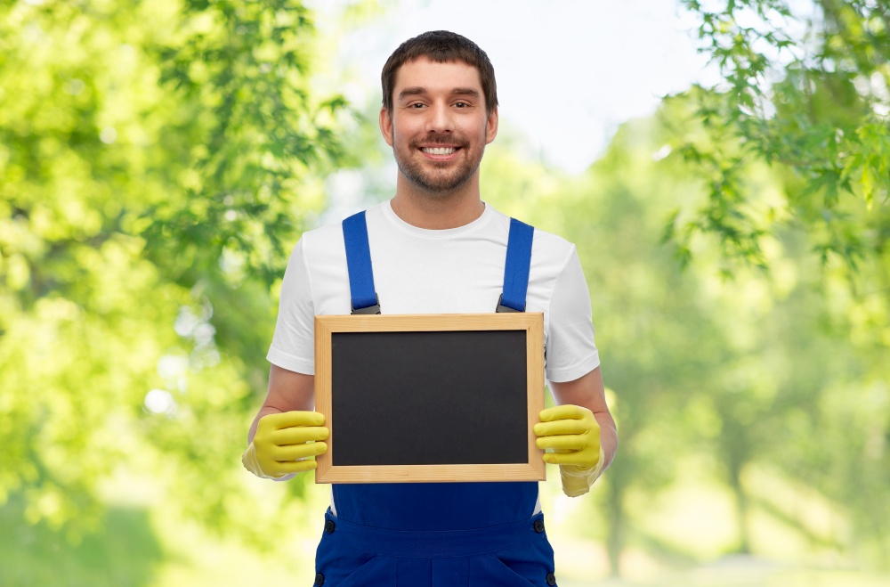 profession, cleaning service and people concept - happy smiling male worker or cleaner showing chalkboard over green natural background. smiling worker or male cleaner showing chalkboard