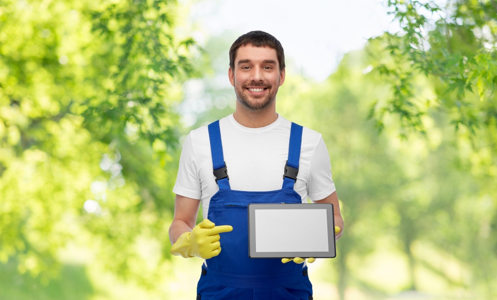 profession, cleaning service and people concept - happy smiling male worker or cleaner in overall and gloves showing tablet pc computer over green natural background. happy male worker or cleaner showing tablet pc