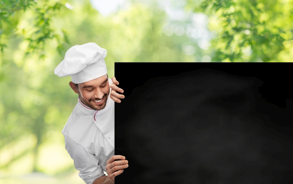 cooking, culinary and people concept - happy smiling male chef in toque with big black chalkboard white board over green natural background. happy smiling male chef with big black chalkboard