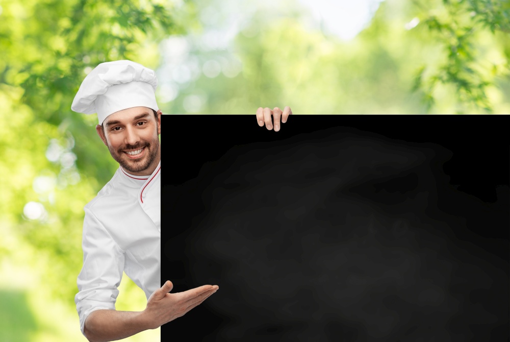 cooking, culinary and people concept - happy smiling male chef in toque with big black chalkboard white board over green natural background. happy smiling male chef with big black chalkboard