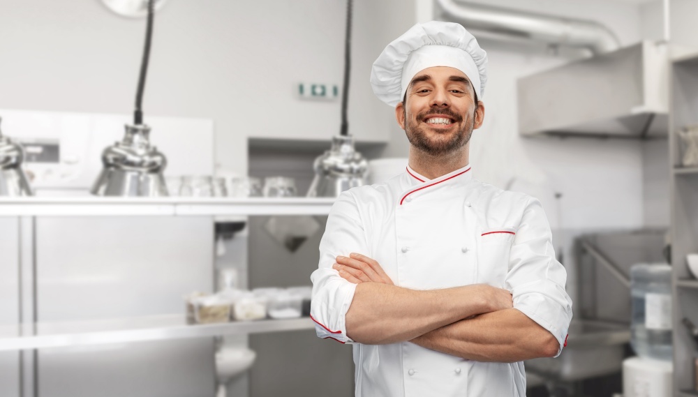 cooking, culinary and people concept - happy smiling male chef in toque and jacket over restaurant kitchen background. happy smiling male chef in toque at kitchen