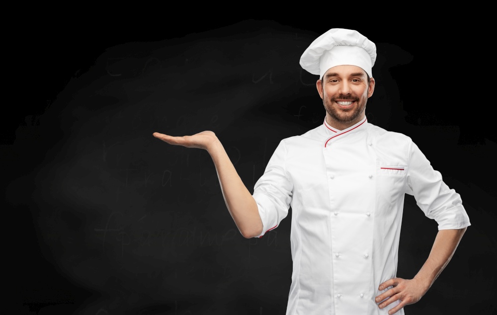 cooking, culinary and people concept - happy smiling male chef in toque holding something on hand over black background. happy smiling male chef holding something on hand