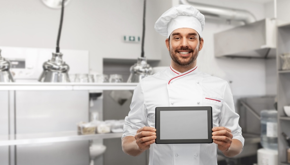 cooking, culinary and people concept - happy smiling male chef in toque showing tablet pc computer over restaurant kitchen background. happy smiling male chef with tablet pc at kitchen