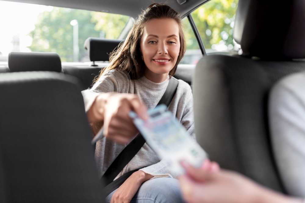 transportation, vehicle and payment concept - female passenger giving money to taxi car driver. female passenger giving money to taxi car driver