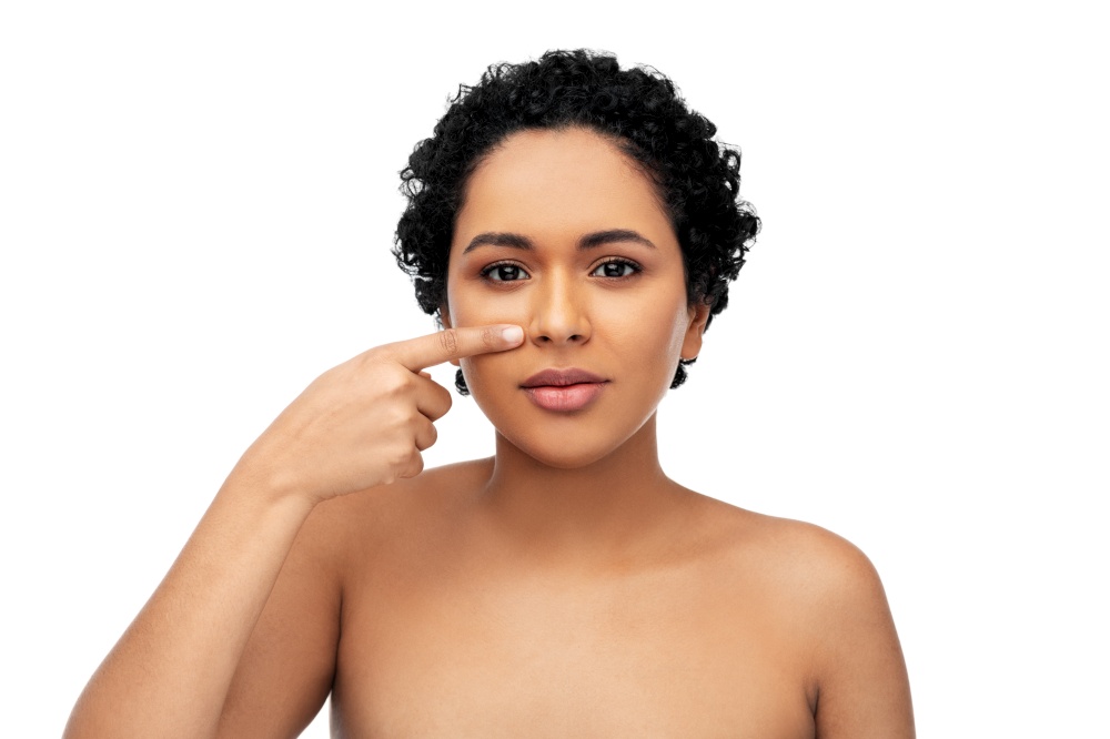 beauty, aesthetic surgery and people concept - portrait of happy smiling young african american woman with bare shoulders pointing to her nose over white background. young african american woman pointing to her nose