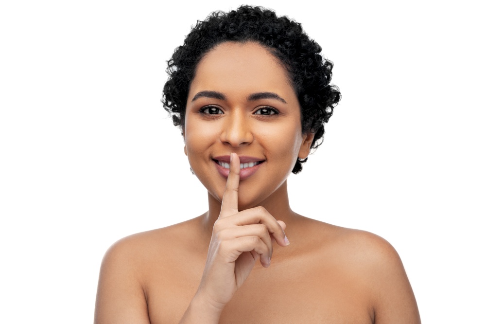 beauty and people concept - portrait of happy smiling young african american woman with finger on lips over white background. young african american woman with finger on lips
