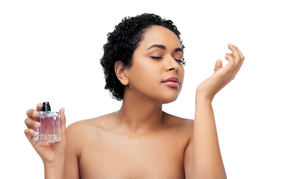 beauty and people concept - portrait of young african american woman with bare shoulders smelling perfume over white background. young african american woman smelling perfume