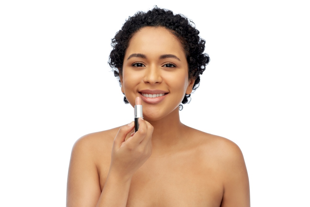 beauty, make up and cosmetics concept - beautiful young african american woman applying lipstick over white background. african american woman applying lipstick