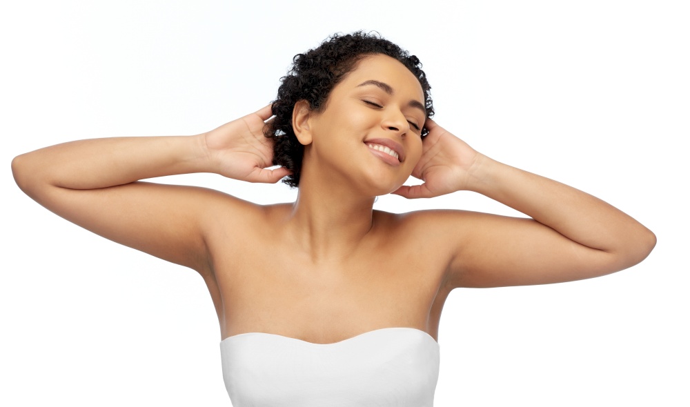 beauty and people concept - portrait of happy smiling young african american woman with bare shoulders touching her hair over white background. portrait of young african american woman