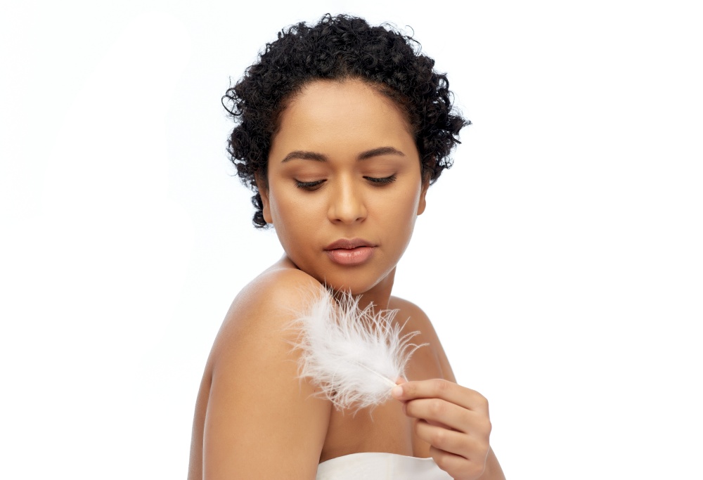 beauty and people concept - portrait of happy smiling young african american woman with bare shoulders and feather over white background. happy african american woman with feather