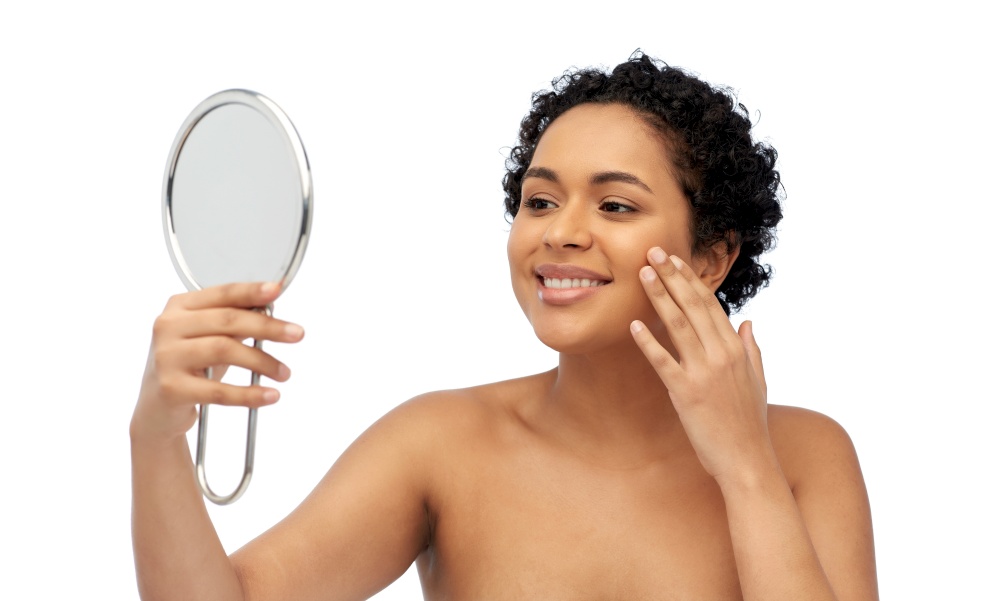 beauty and people concept - portrait of happy smiling young african american woman with bare shoulders looking to mirror over white background. smiling african american woman looking to mirror