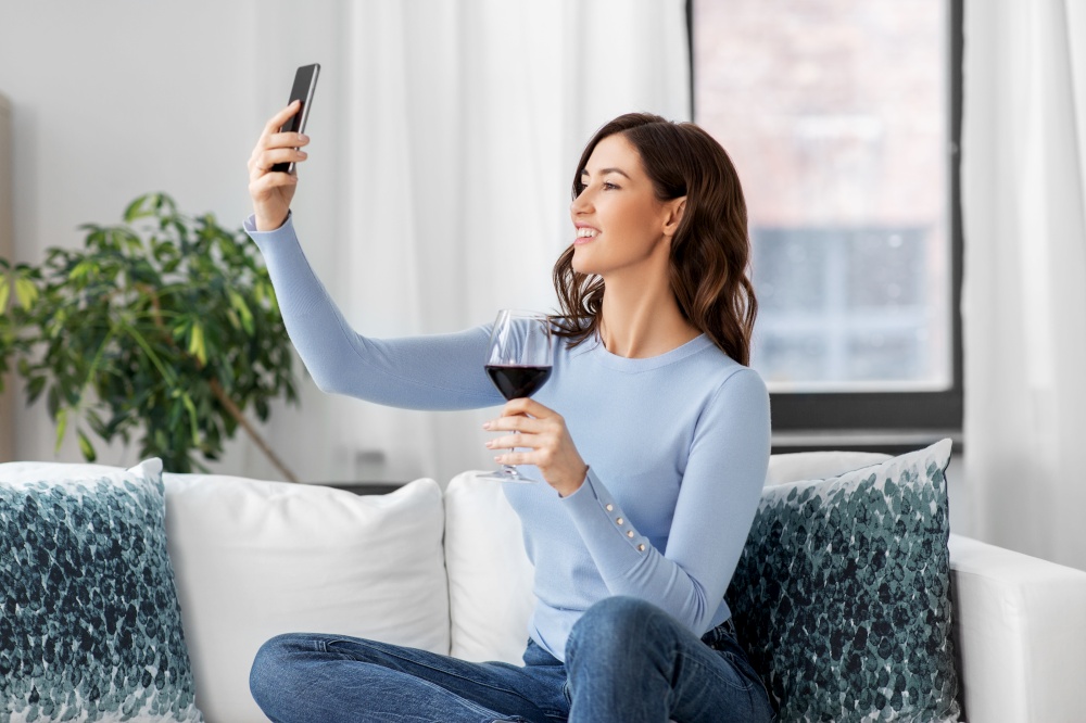 leisure and people concept - happy woman with smartphone taking selfie and drinking red wine at home. woman with smartphone and wine taking selfie