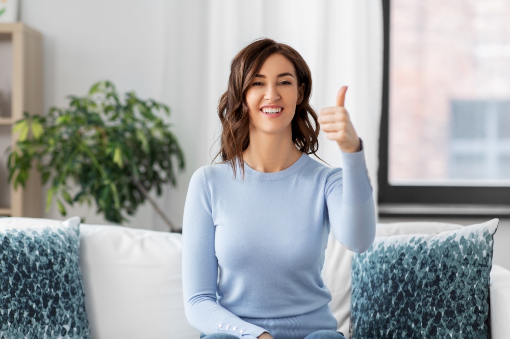 people, ethnicity and portrait concept - happy young woman showing thumbs up at home. happy woman showing thumbs up at home