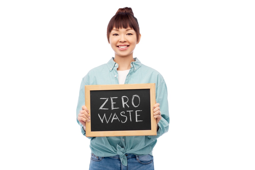 eco living, environment and sustainability concept - portrait of happy smiling young asian woman in turquoise shirt holding chalkboard with zero waste words grey background. asian woman holds chalkboard with zero waste words