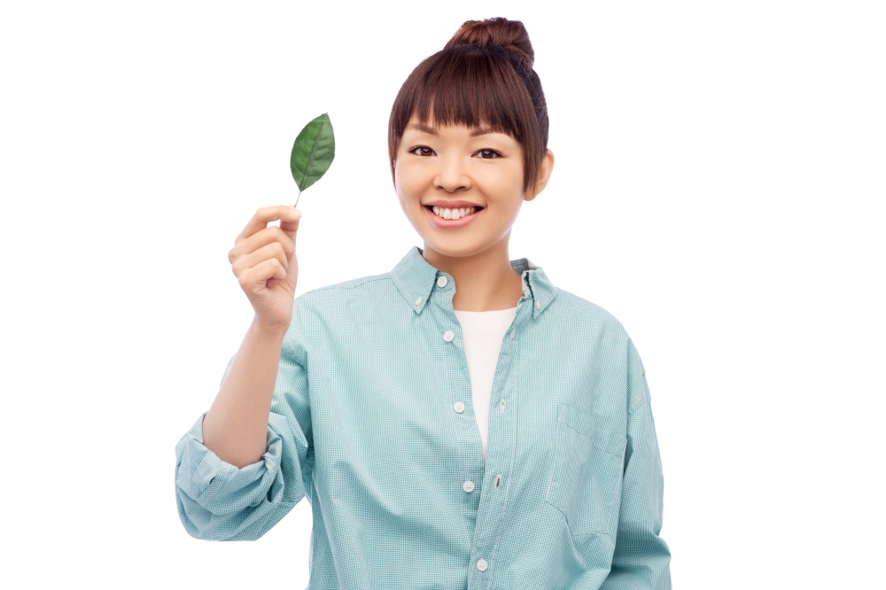 eco living, environment and sustainability concept - portrait of happy smiling young asian woman in turquoise shirt holding green leaf over white background. smiling asian woman holding green leaf