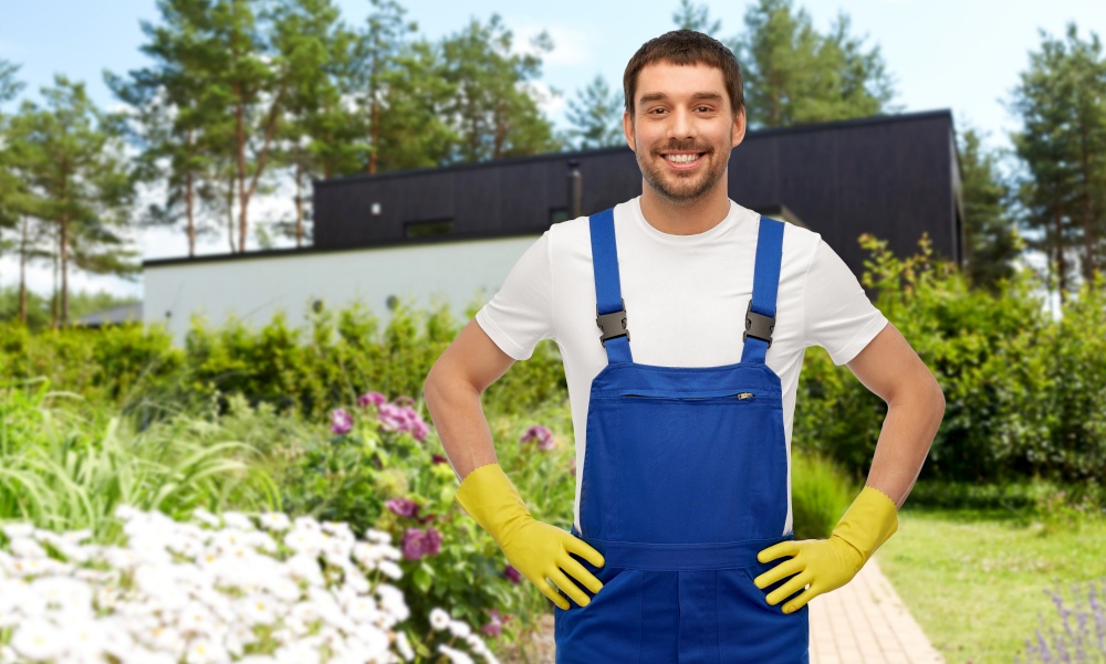 profession, cleaning service and building concept - happy smiling male worker or cleaner in overall and gloves over summer garden background. happy male worker or cleaner in gloves at garden