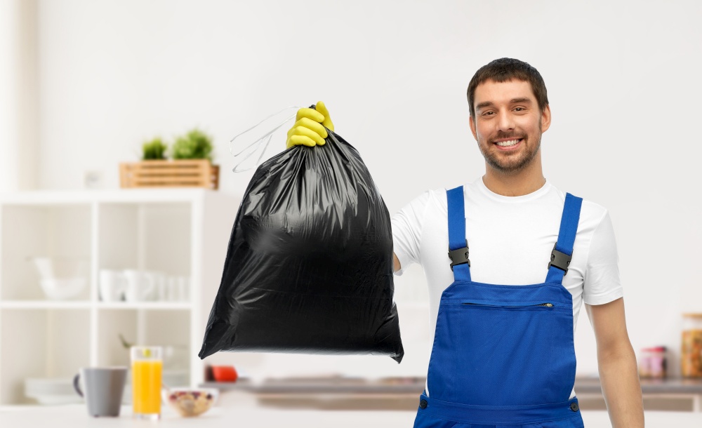 profession, cleaning service and people concept - happy smiling male worker or cleaner in overall and gloves showing garbage bag over home room background. male cleaner showing garbage bag at home kitchen