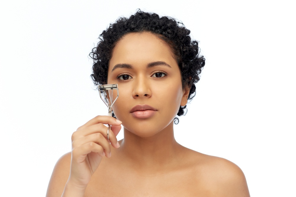 beauty, make up and cosmetics concept - young african american woman with eyelash curler over white background. african american woman with eyelash curler
