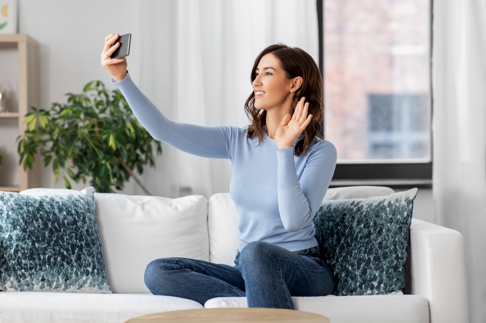 technology and people concept - happy smiling woman with smartphone and taking selfie or having video call sitting on sofa at home. happy woman with smartphone taking selfie at home
