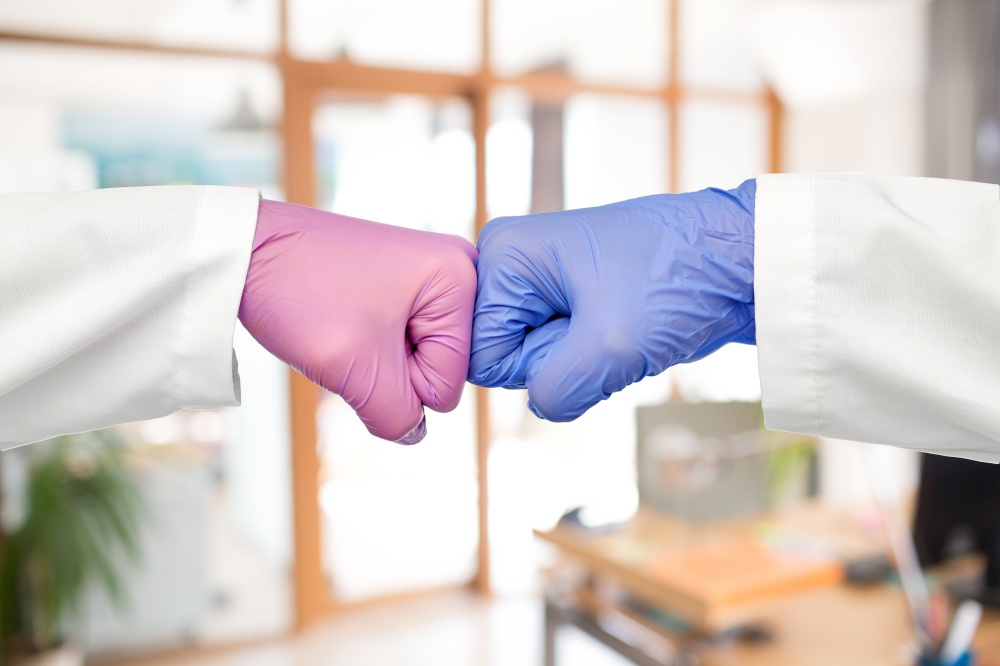 medicine, health protection and healthcare concept - hands of doctors in gloves make fist bump gesture over office background. hands of doctors in gloves make fist bump gesture