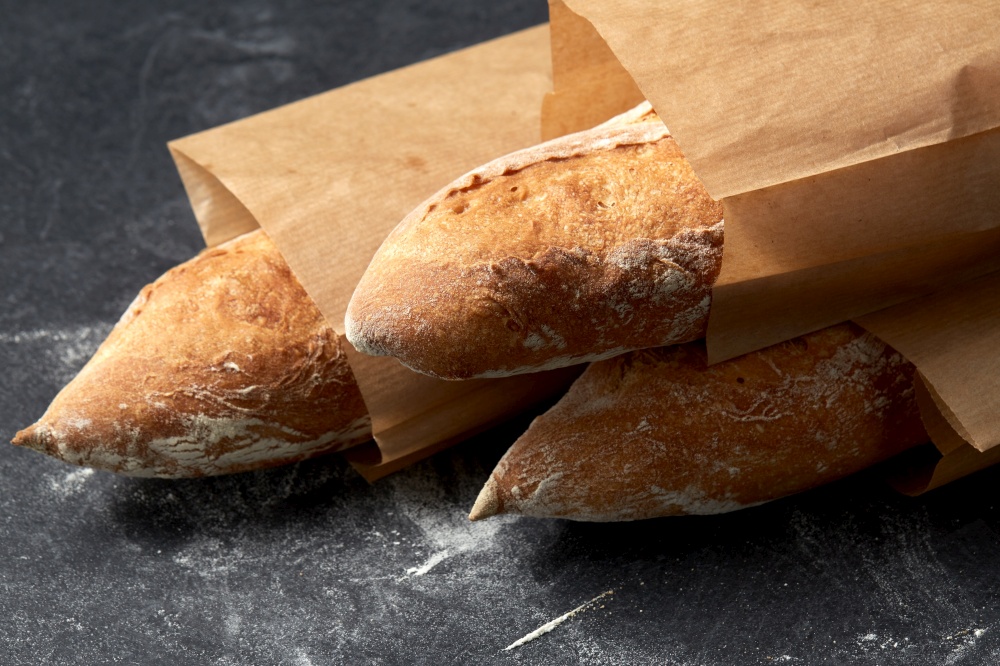 food, baking and cooking concept - close up of baguette bread in paper bags on table over dark background. close up of baguette bread in paper bags on table