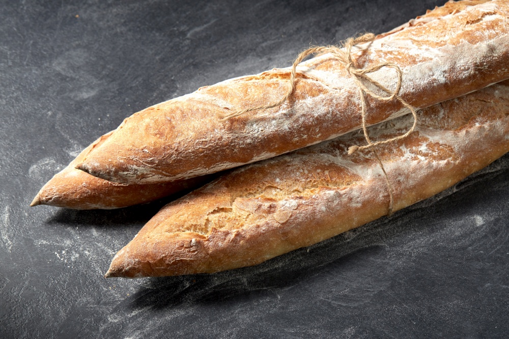food, baking and cooking concept - pile of baguette bread loaves tied with rope on table over dark background. pile of baguette bread loaves tied with rope