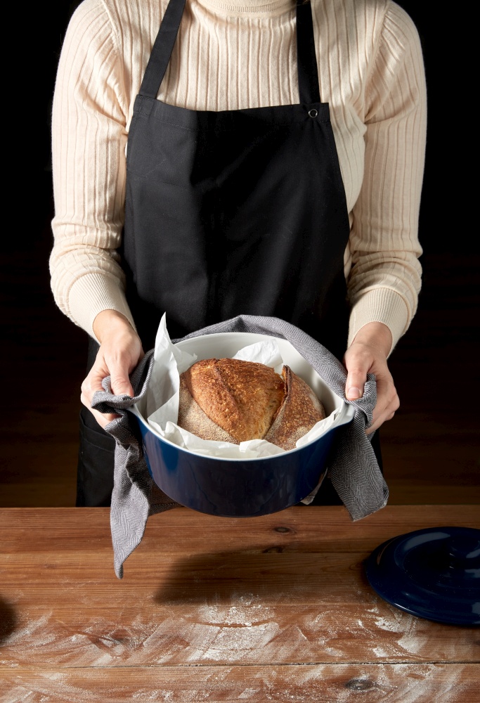food cooking and people concept - female baker with loaf of bread in baking dish at bakery or kitchen. female baker with homemade bread at bakery