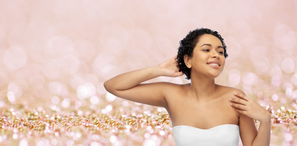 beauty and people concept - portrait of happy smiling young african american woman with bare shoulders touching her hair over pink glitter background. portrait of young african american woman