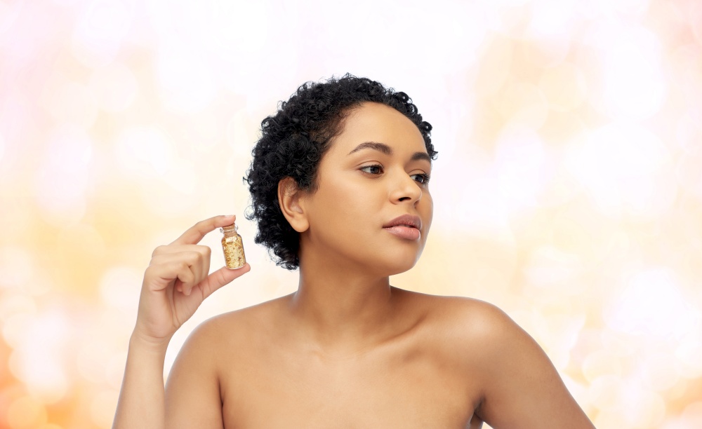 beauty and people concept - portrait of young african american woman with gold facial mask in bottle over lights background. african american woman with gold mask in bottle