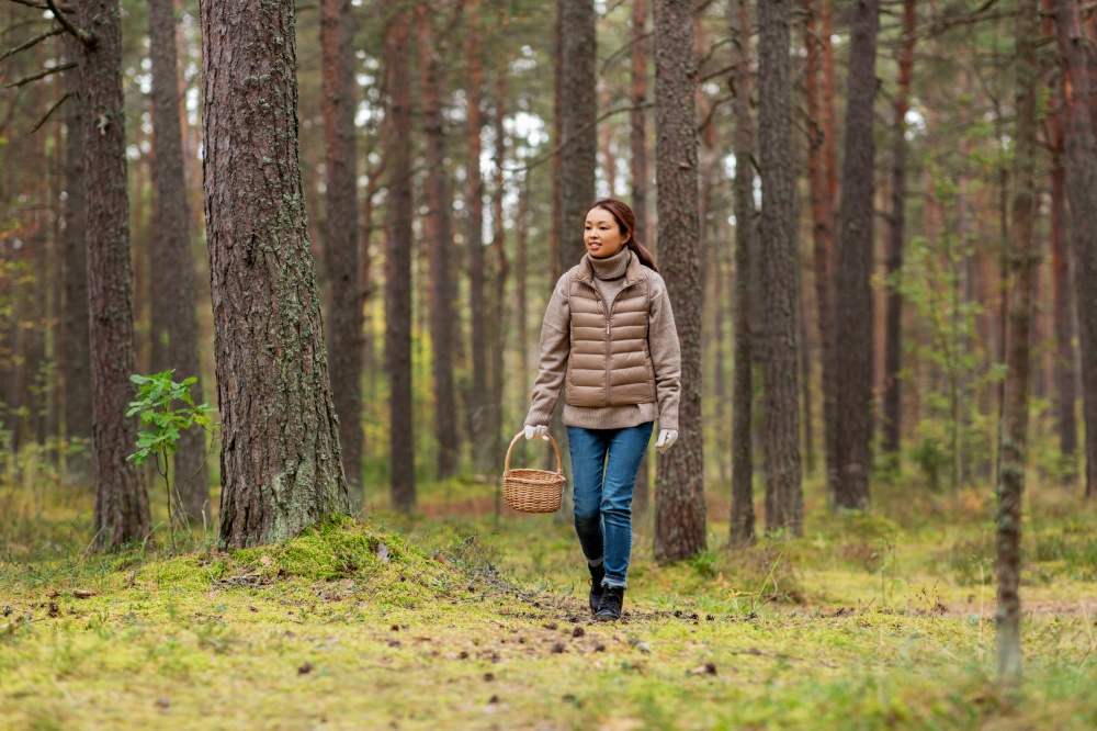 picking season, leisure and people concept - young asian woman with mushrooms in basket walking in autumn forest. young woman picking mushrooms in autumn forest