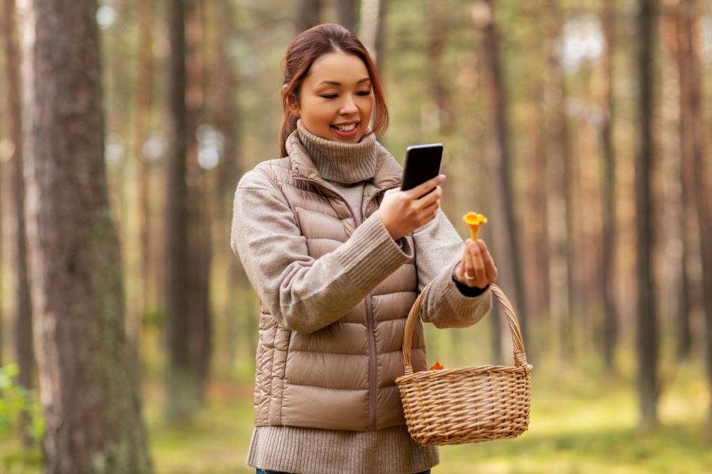 technology, leisure and people concept - young asian woman with smartphone using app to identify mushroom in autumn forest. asian woman using smartphone to identify mushroom