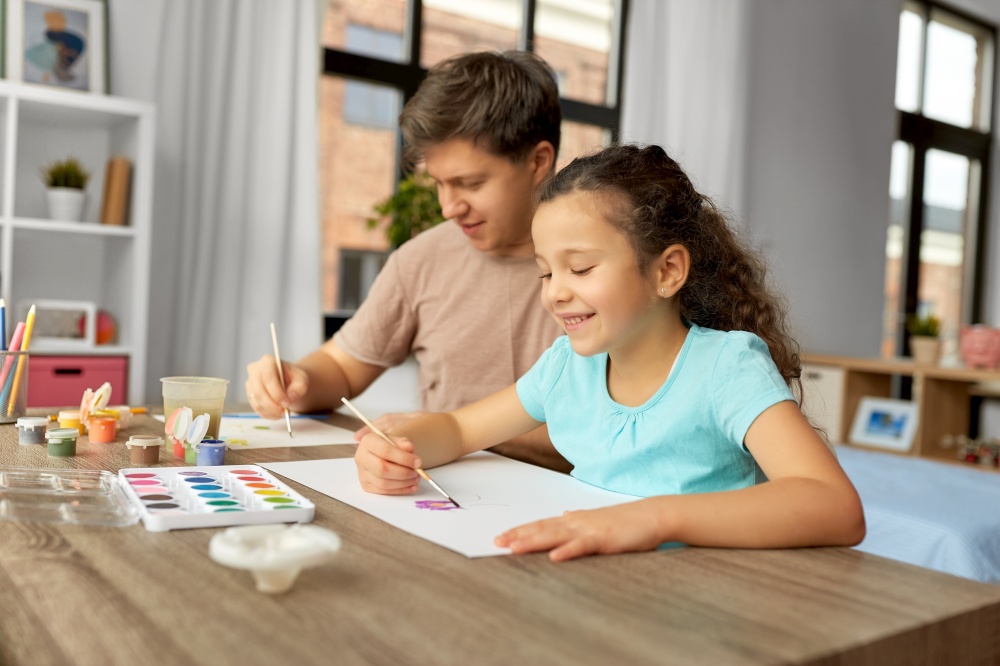 family, motherhood and leisure concept - happy smiling father spending time with his little daughter and drawing with colors at home. happy father with little daughter drawing at home