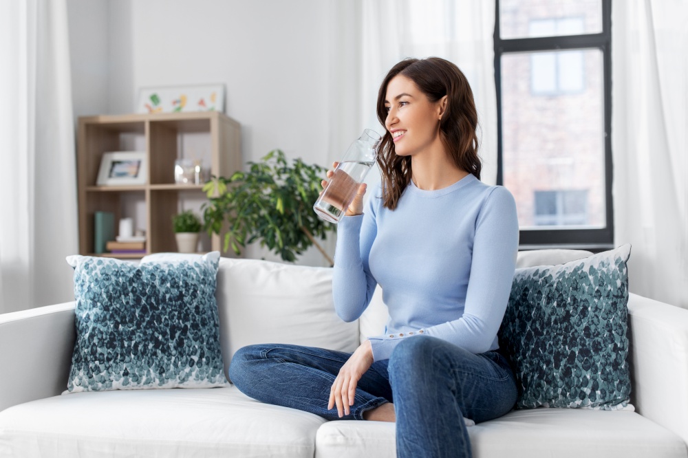 people, sustainability and leisure concept - happy smiling young woman drinking water from glass bottle at home. woman drinking water from glass bottle at home